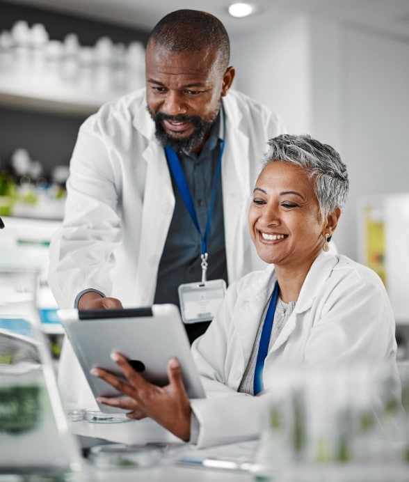 Image of a man and a woman with lab coats smiling while looking at a tablet in a laboratory